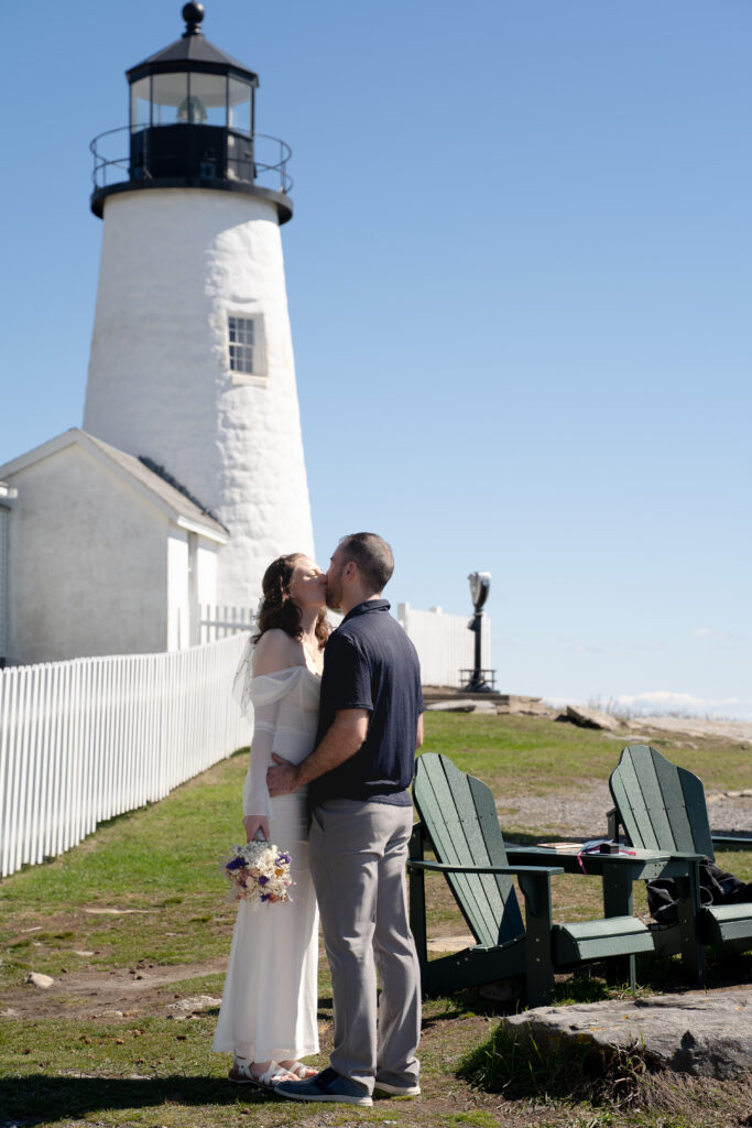  Bride and groom standing on rocky cliffs during a spring elopement at Pemaquid Point Lighthouse overlooking the Atlantic