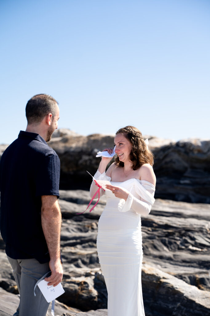 Bride and groom walking along rocky cliffs at Pemaquid Point Lighthouse during a spring wedding in coastal Maine