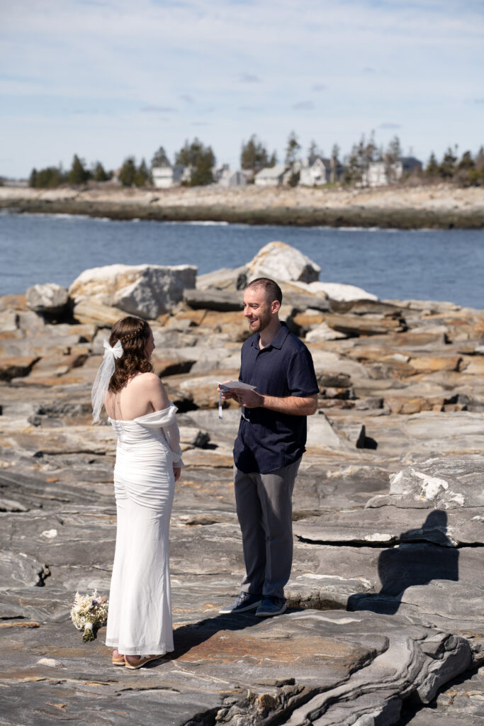 Couple embracing during a spring elopement at Pemaquid Point Lighthouse overlooking rocky shores and Atlantic Ocean