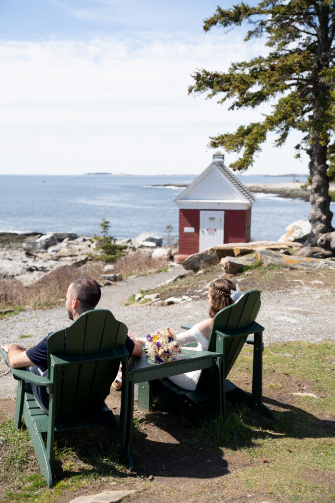 Couple sitting along rocky shoreline during spring elopement at Pemaquid Point Lighthouse in coastal Maine

