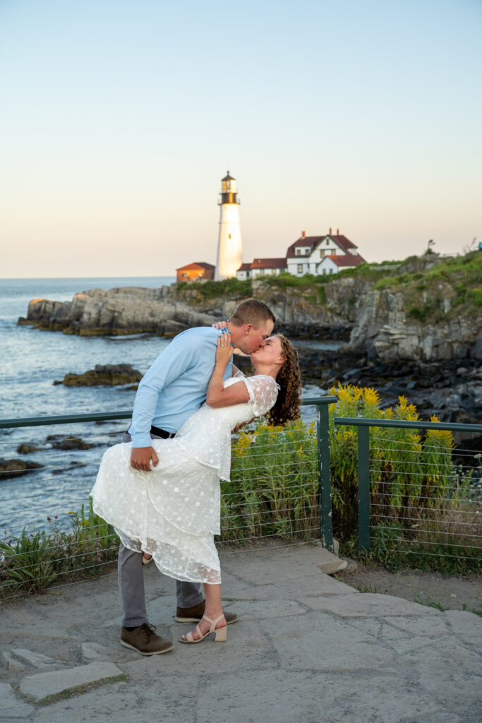 Bride and groom standing on rocky cliffs beside Portland Head Light during a summer elopement with bright ocean views

