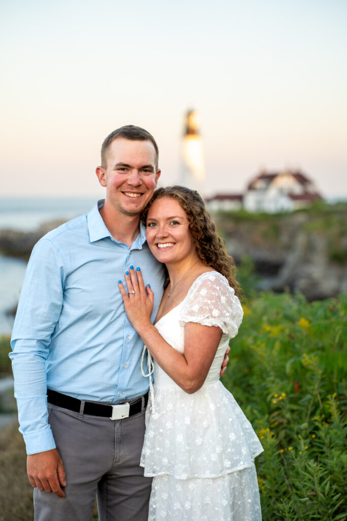 Intimate summer wedding portraits at Portland Head Light with rugged shoreline and sparkling Atlantic waters behind the couple