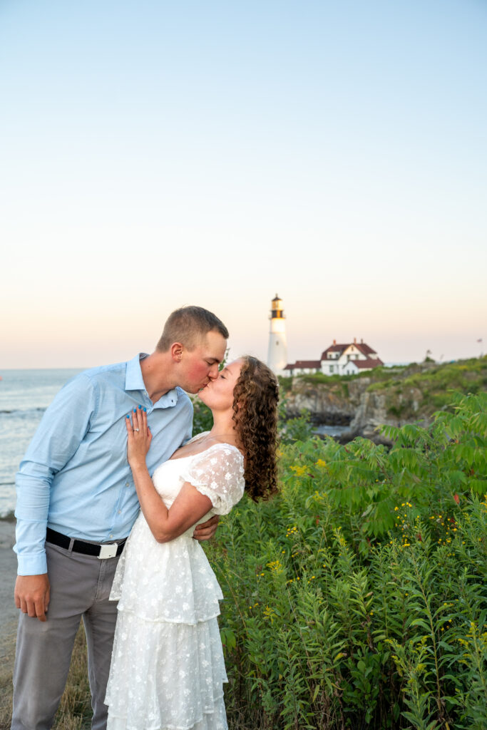 Couple standing together at Portland Head Light during sunset elopement with warm light reflecting off the Maine coastline